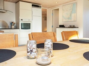 A dining table with three glass jars containing seashells, wooden chairs, and a white cabinet in the background. - 4 Person Holiday Home in Hals (Hals)