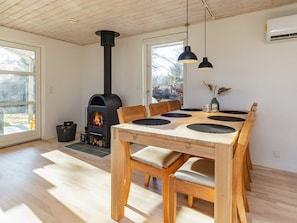 Ein modernes Interieur mit Kaminofen, Esstisch mit schwarzen Platzsets, Holzsesseln und Pendelleuchten.