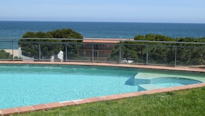 Ein Schwimmbad mit freiem Blick auf das Meer und ein Gebäude mit rotem Dach im Hintergrund.