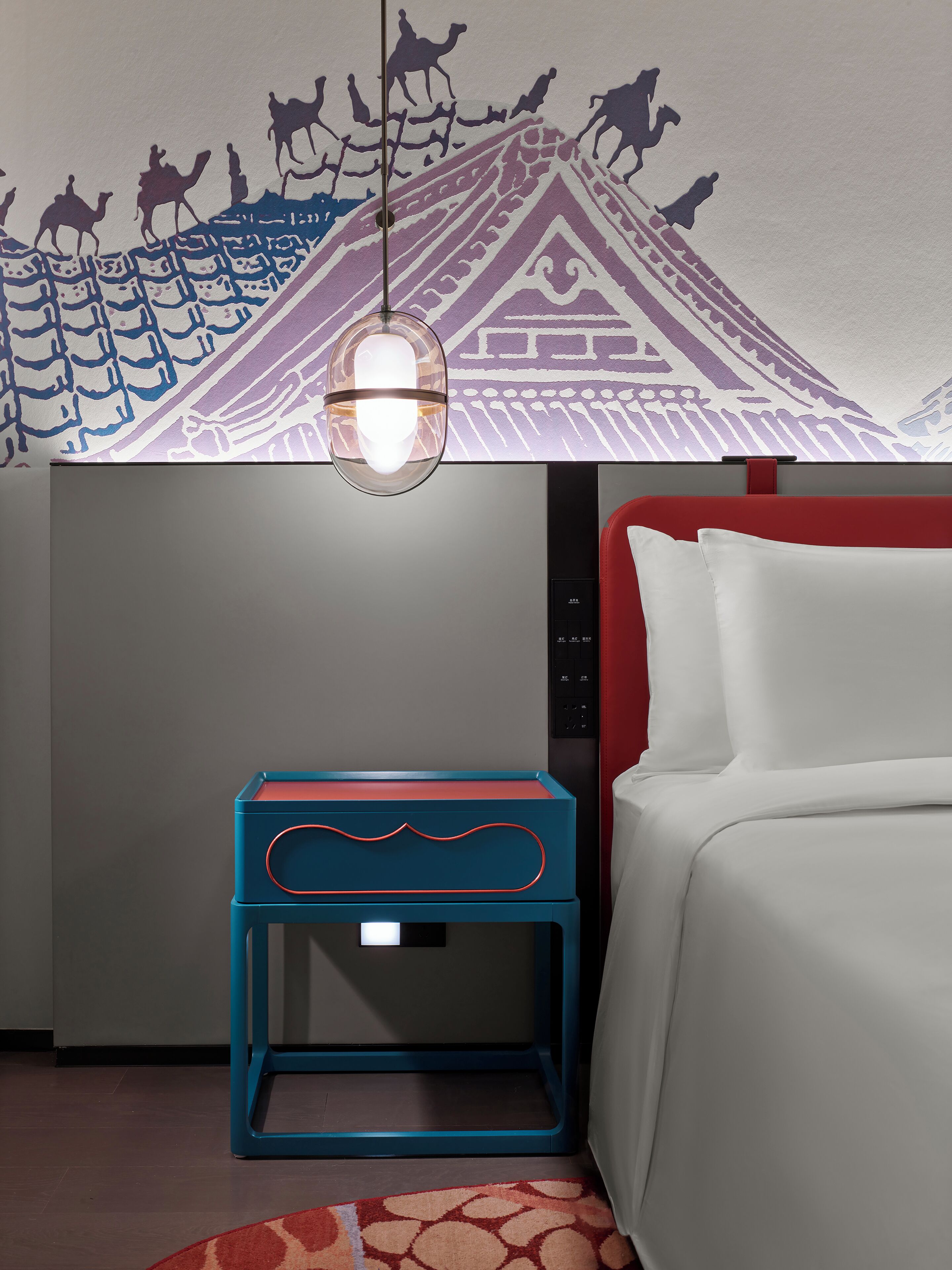 Une chambre d’hôtel avec un lit, une table de chevet, une fresque murale et un luminaire suspendu.