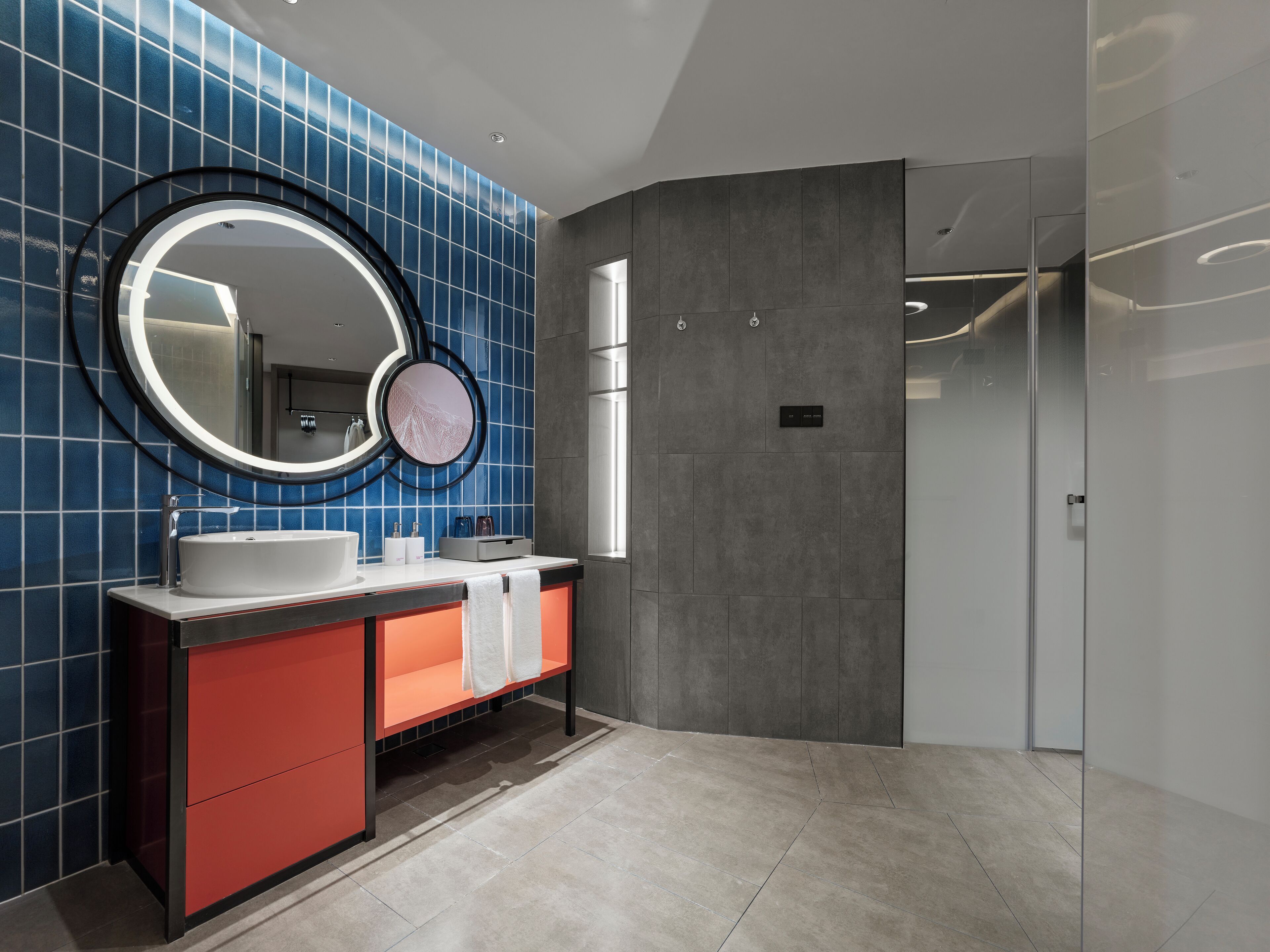 Un baño moderno con un espejo grande, dos lavamanos y un tocador rojo.