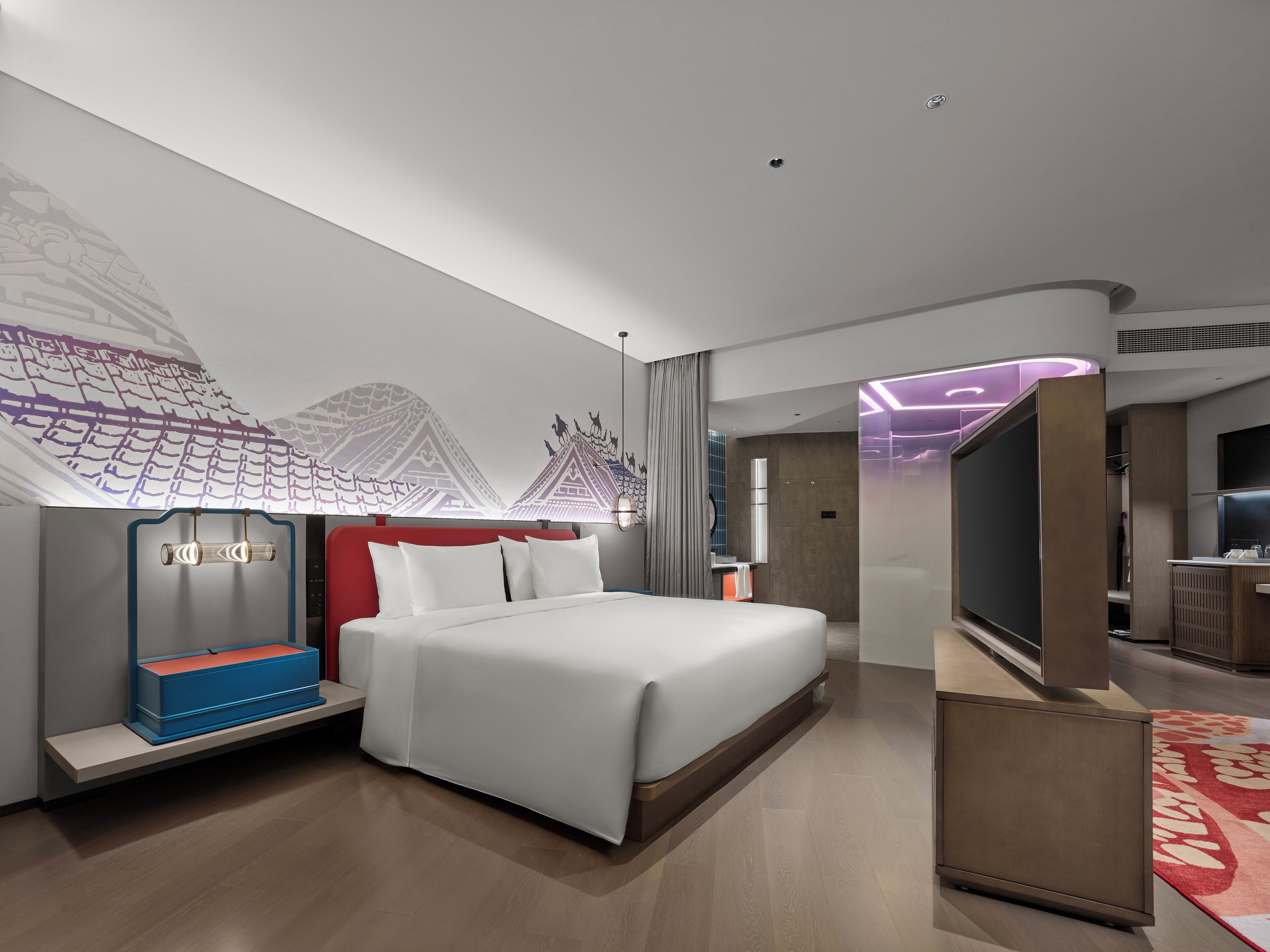 A modern hotel room with a large bed, a TV, a desk, and a bathroom visible through an open door.