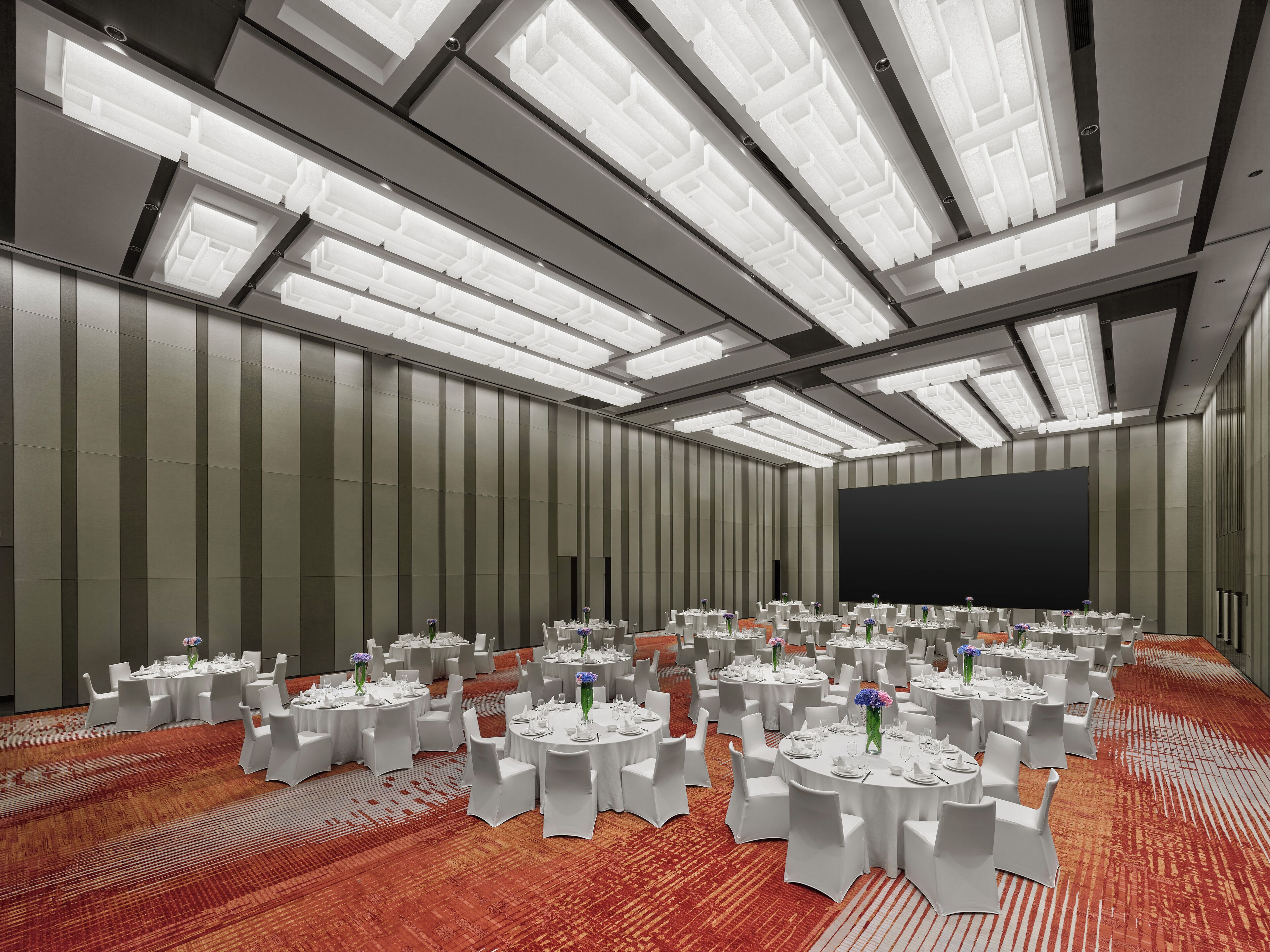 A large conference room with multiple round tables, white chairs, and a carpeted floor.