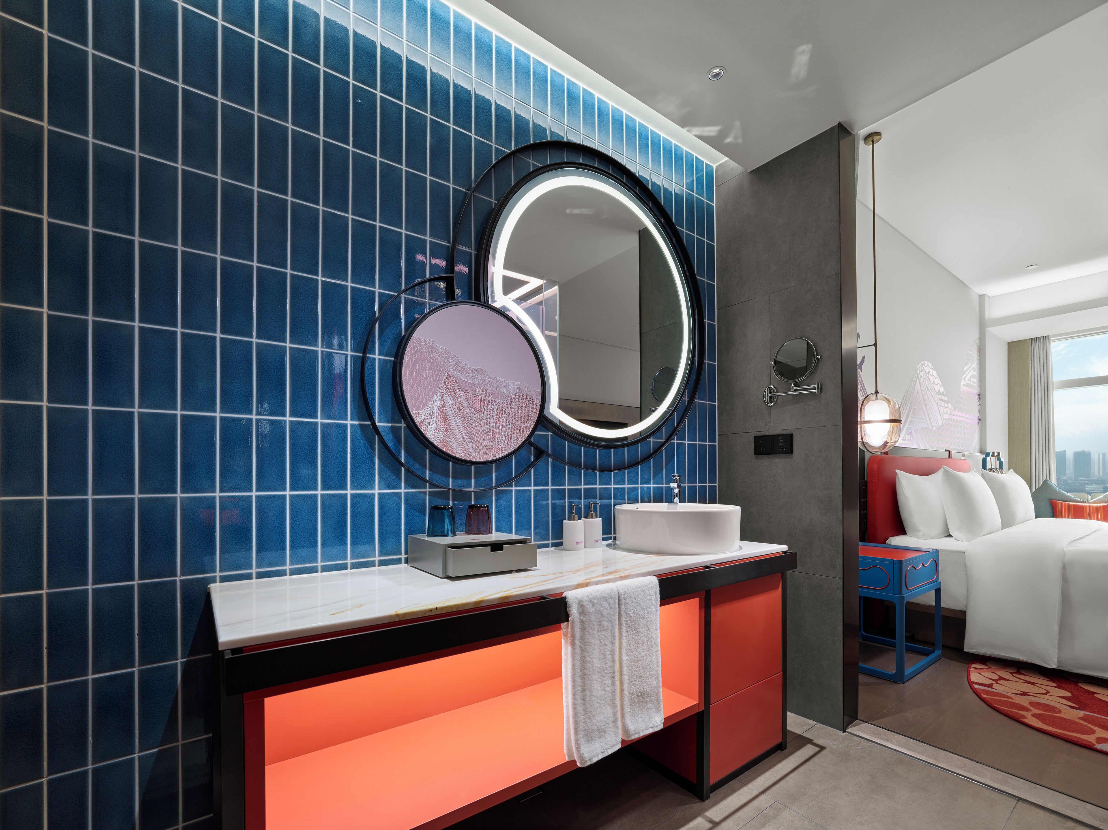 A modern bathroom with blue tiles, a round mirror, a white sink, and a red vanity.
