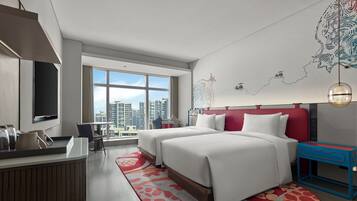 A modern hotel room with two beds, a desk, a TV, and large windows offering a city view.