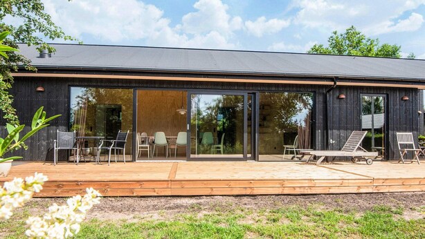 A modern house with a large sliding glass door, a wooden deck, and outdoor seating. - 6 Person Holiday Home in Juelsminde-by Traum (Juelsminde)