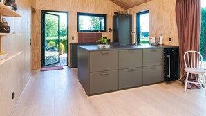 A modern kitchen with wooden walls, a large island, and a view of the garden. - 6 Person Holiday Home in Juelsminde-by Traum (Juelsminde)