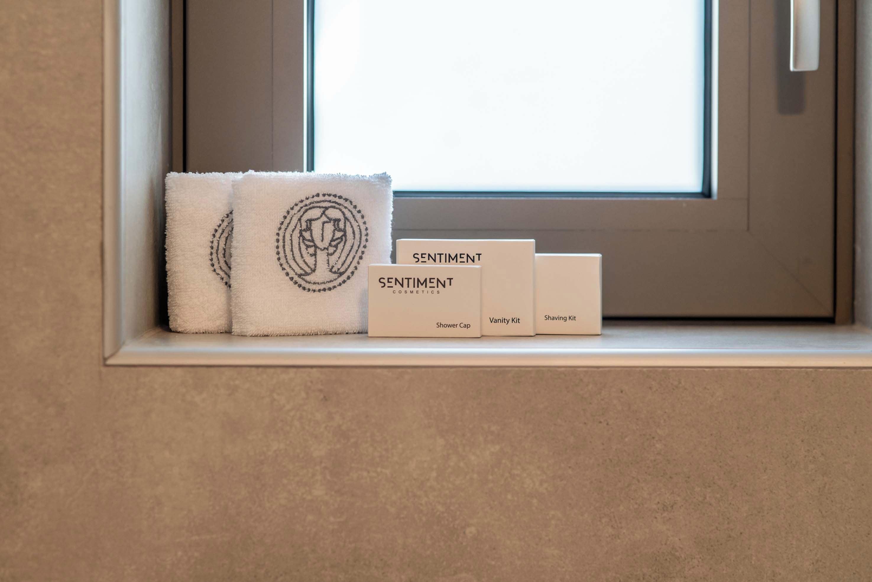 Ein Fenster mit einem Handtuch und drei Toilettenartikeln auf einem Regal, wobei die Kosmetikprodukte mit 'Sentiment Cosmetics' beschriftet sind.
