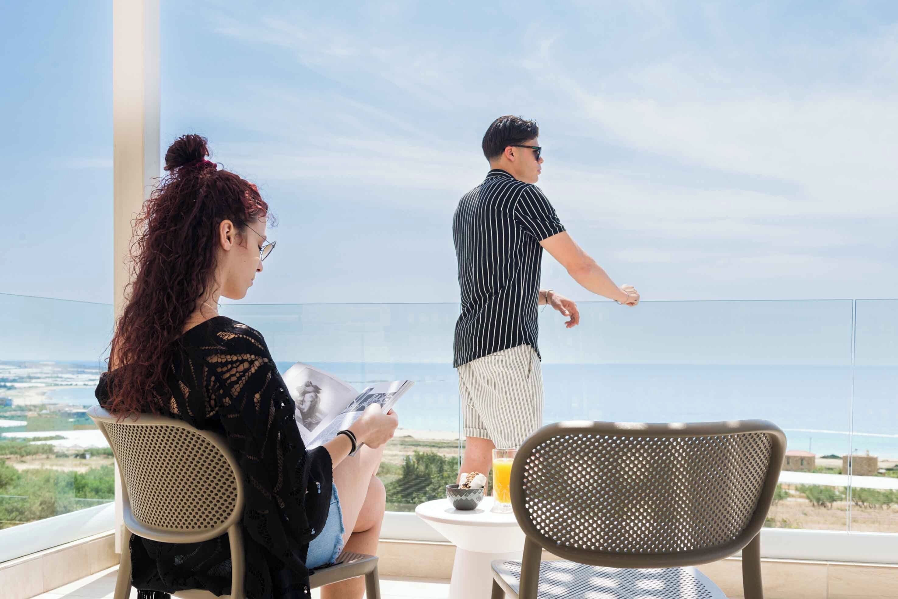 A balcony with two chairs, a table, and a view of the sea.