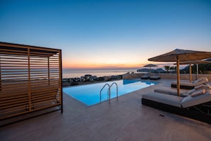 An infinity pool with a view of the sea at sunset, outdoor seating, and a wooden pergola. - Actea Seaview Villas - Holiways Collection (Kissamos)