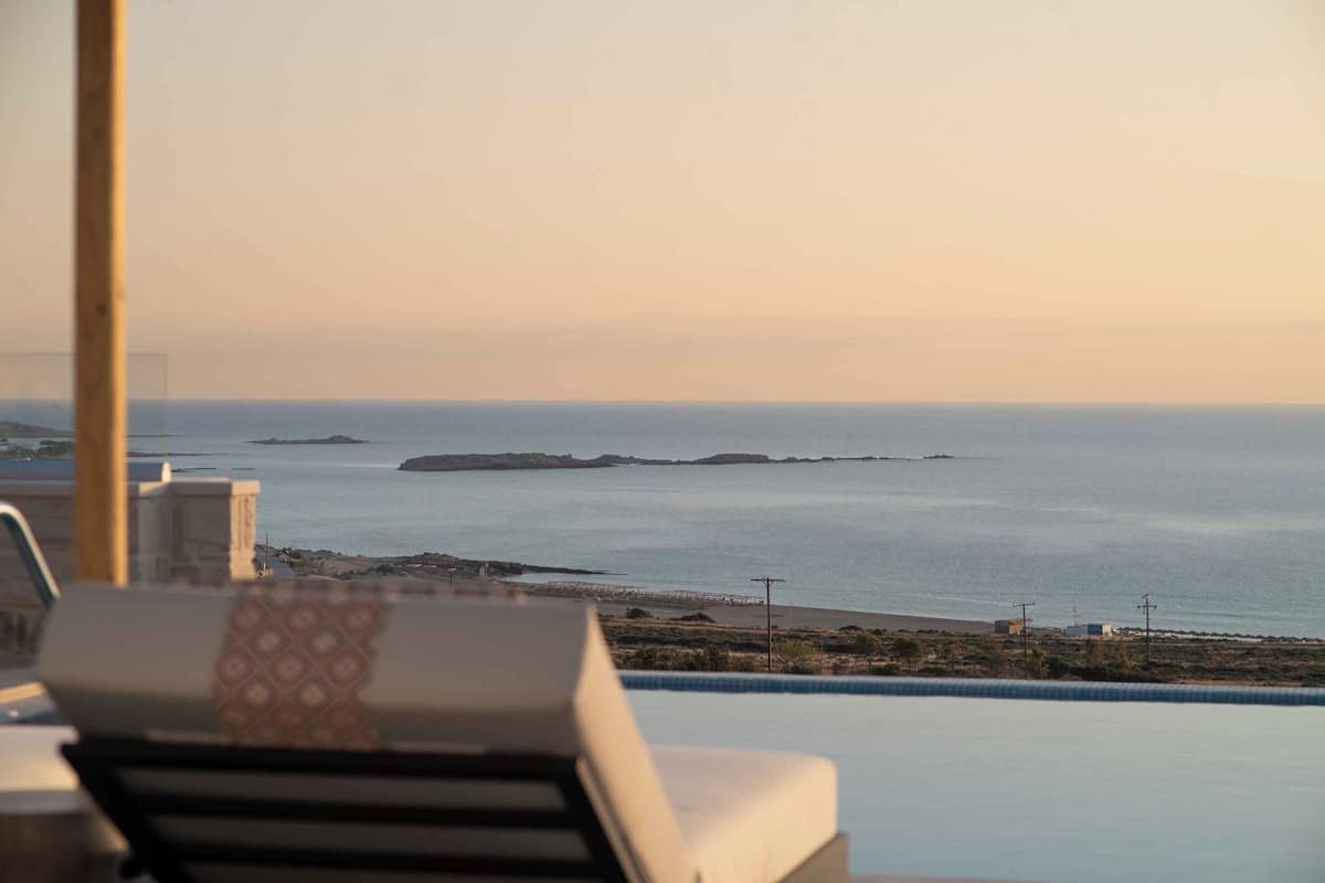 Vista de uma varanda com vista para uma praia, piscina e espreguiçadeiras.