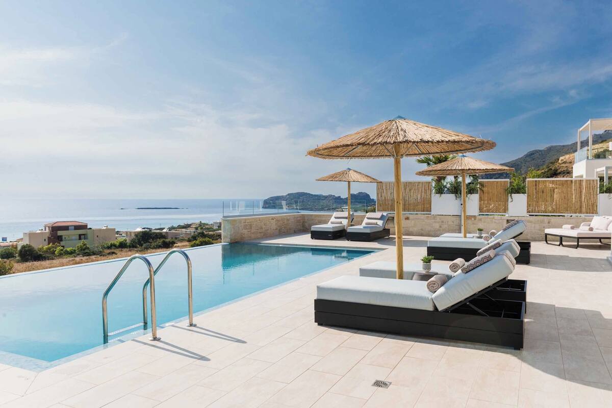Uma área de piscina no terraço com vista clara para o mar, cadeiras de descanso e guarda-sóis.