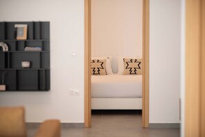 A room with a bed, a wooden door, and a black shelving unit against the wall. - Actea Seaview Villas - Holiways Collection (Kissamos)