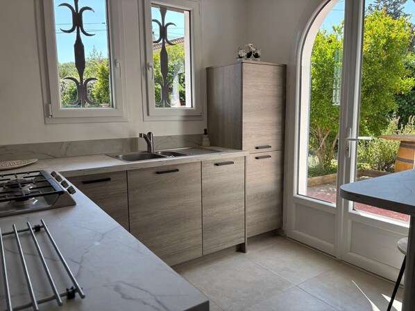A modern kitchen with a gas stove, double sink, and light wood cabinets.