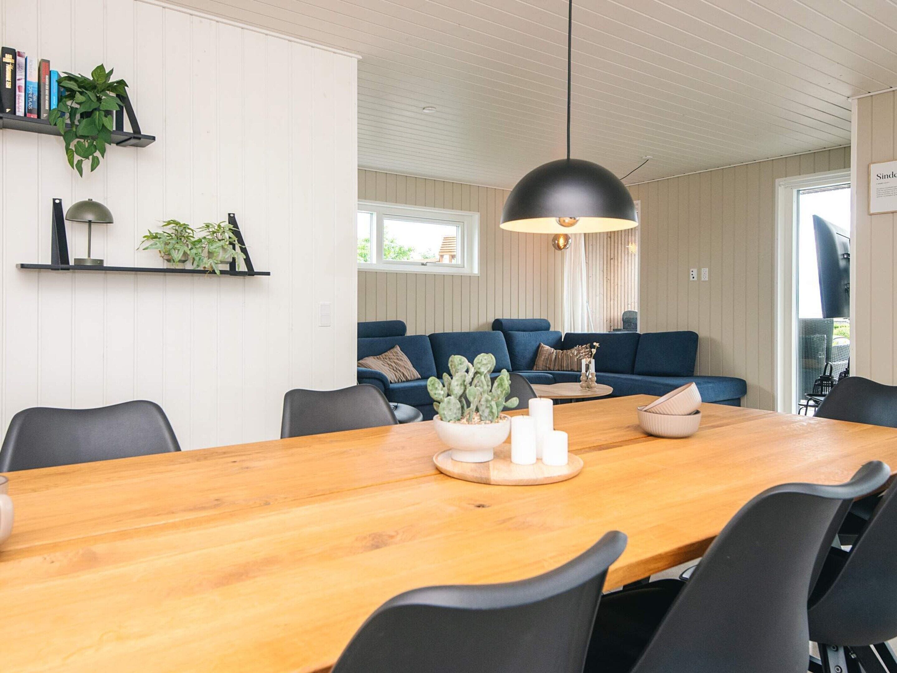 A modern living room with a wooden dining table, black chairs, a blue sofa, and a hanging black pendant light.