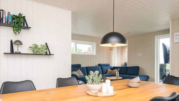 A modern living room with a wooden dining table, black chairs, a blue sofa, and a hanging black pendant light. - 5 Star Holiday Home in Haderslev (Haderslev)