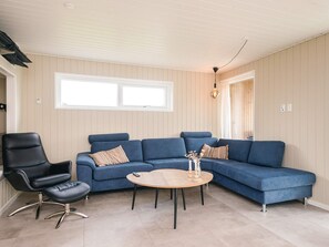 A living room with a blue sofa, a black chair, and a round wooden table. - 5 Star Holiday Home in Haderslev (Haderslev)