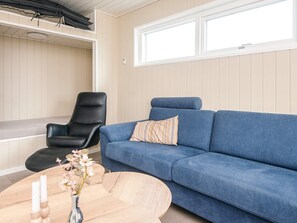 A living room with a blue sofa, a black leather chair, a wooden coffee table, and a window with blinds.
