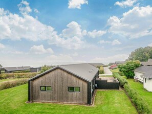 A large wooden barn with a metal roof, surrounded by well-maintained grass and hedges, with a clear sky above.