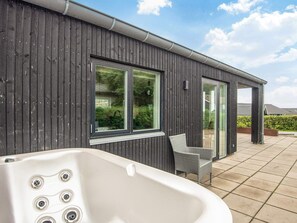 A modern building with a wooden exterior, a hot tub, and a patio area with a chair. - 9 Person Holiday Home in Haderslev (Haderslev)
