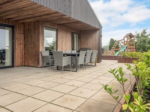 A modern outdoor patio with a dining table and chairs, a barbecue grill, and a children's play structure. - 9 Person Holiday Home in Haderslev (Haderslev)