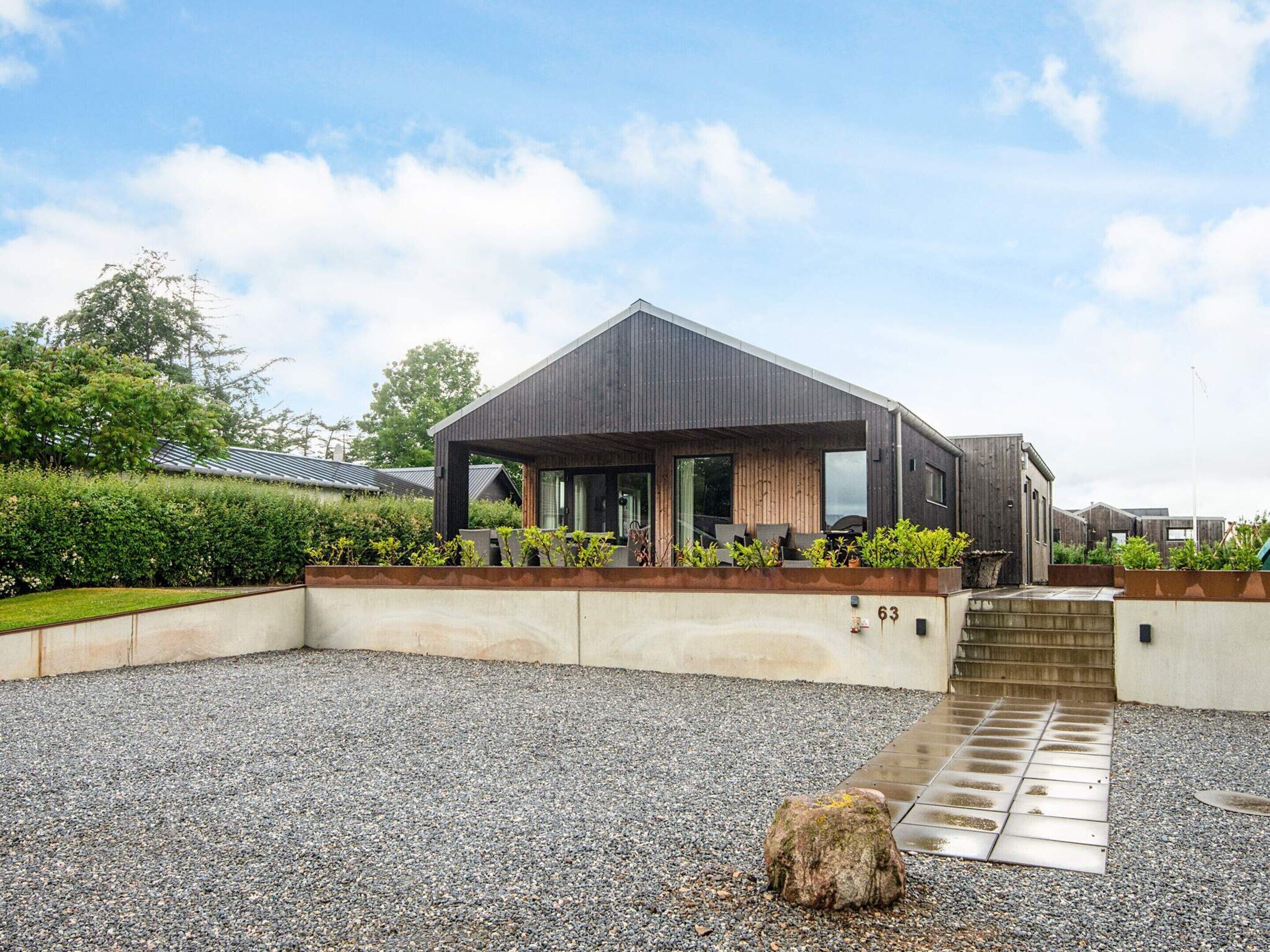 A modern house with a covered patio, a gravel driveway, and a number 63 sign.