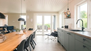 A modern kitchen with a wooden dining table, black chairs, a grey cabinet, and a large window. - 5 Star Holiday Home in Haderslev (Haderslev)