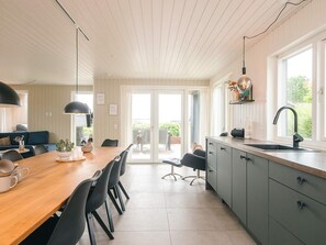 A modern kitchen with a wooden dining table, black chairs, a grey cabinet, and a large window. - 5 Star Holiday Home in Haderslev (Haderslev)