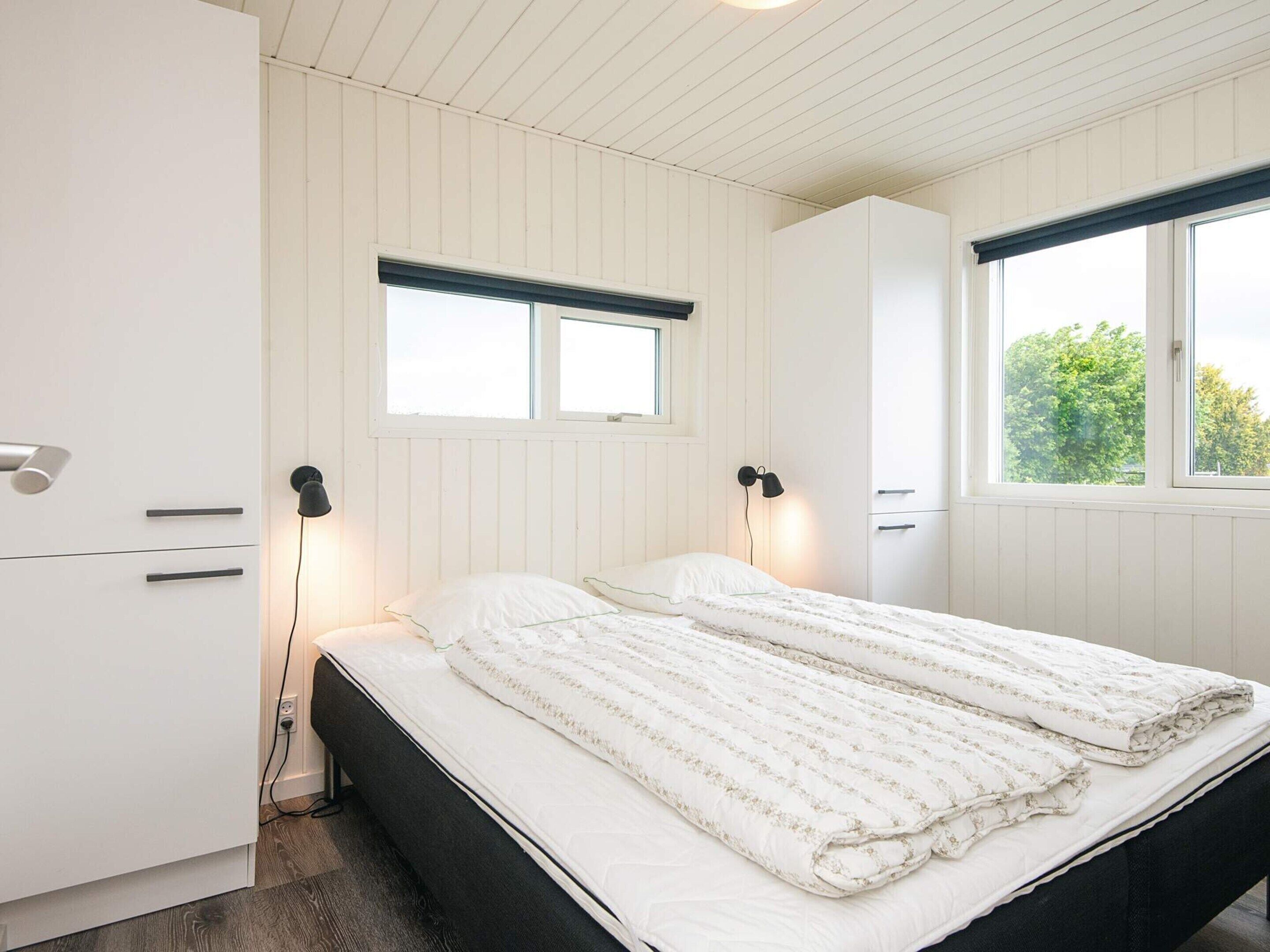 A bedroom with a bed, two bedside tables, a wardrobe, and a window with a view of greenery.