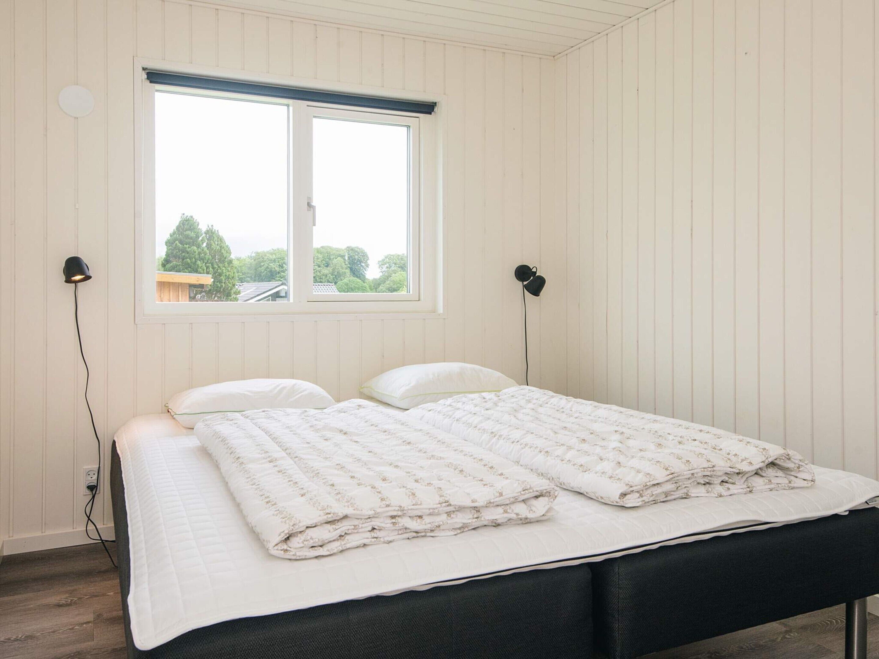 A bedroom with a bed, two bedside lamps, a window, and a view of trees.