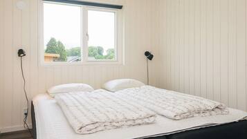 A bedroom with a bed, two bedside lamps, a window, and a view of trees.