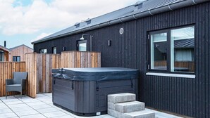 A modern building with a dark exterior, a hot tub, and a wooden deck. - 5 Star Holiday Home in Haderslev (Haderslev)