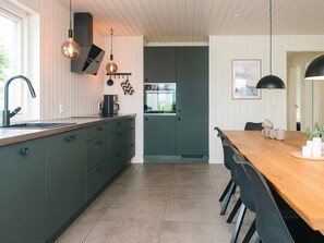A modern kitchen with a central island, a dining area with a wooden table and chairs, and a view into the adjacent dining room. - 9 Person Holiday Home in Haderslev (Haderslev)