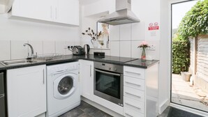 Une cuisine moderne avec des armoires blanches, un lave-linge intégré, un four et une hotte de cuisinière en acier inoxydable.