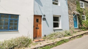 Un bâtiment à deux étages, doté d’une façade blanche et d’un mur en pierre. On y trouve une porte en bois surmontée d’une enseigne, une antenne parabolique et une fenêtre avec des volets bleus.