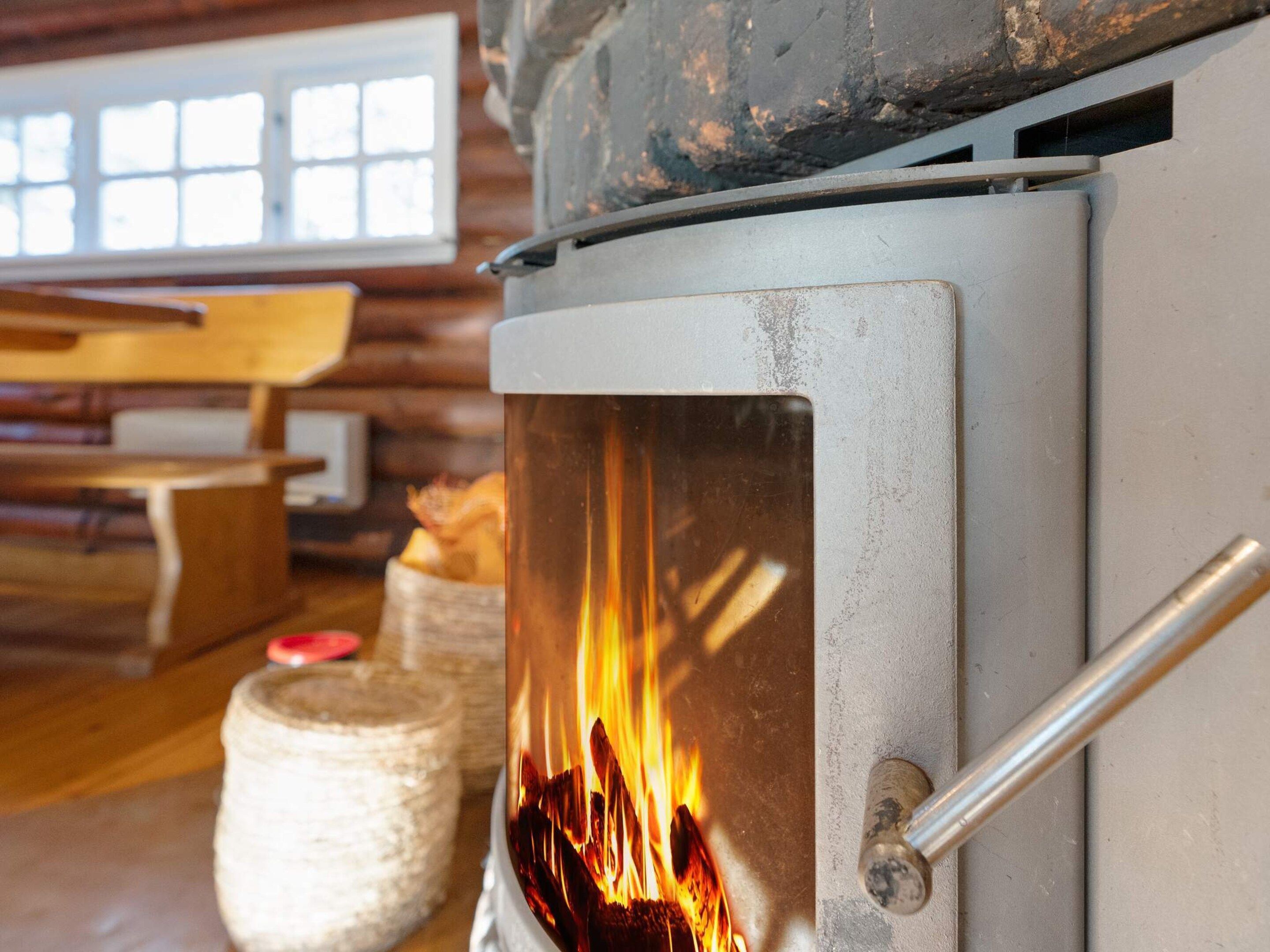 Ein Kaminofen mit sichtbaren Flammen, ein Fenster mit Jalousien und ein rustikales Interieur.