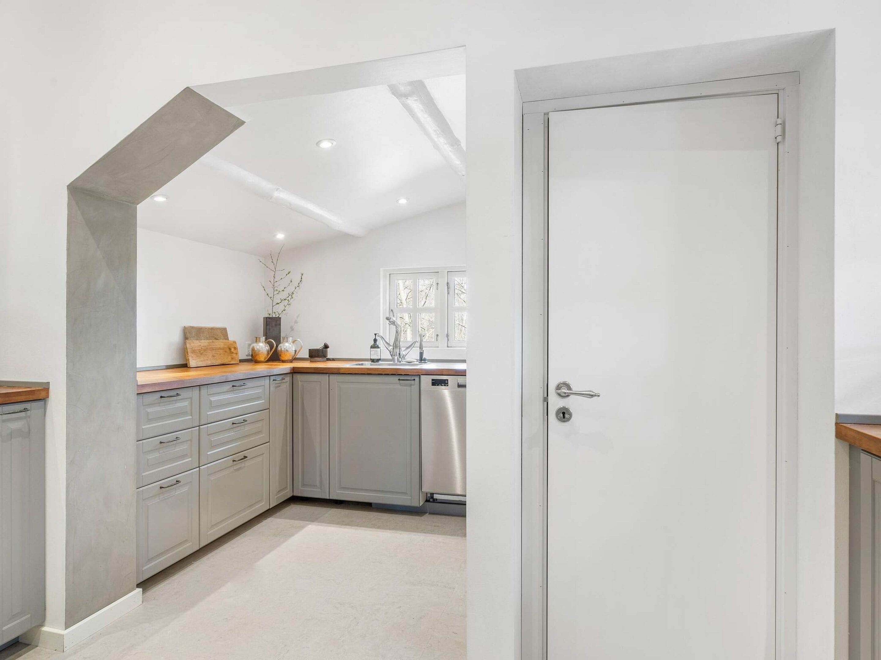 A modern kitchen with grey cabinets, a wooden countertop, and a stainless steel dishwasher.