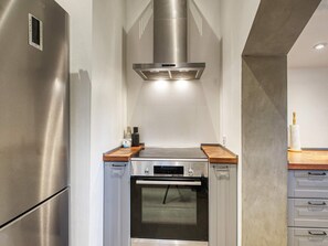 Cocina compacta con refrigerador de acero inoxidable, horno Bosch y extractor moderno.