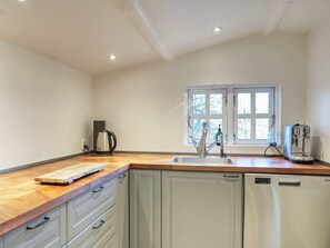 A kitchen with a wooden countertop, a sink, a kettle, a toaster, and a window with a view of trees.