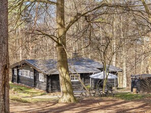 A log cabin with a sloped roof, surrounded by trees and a dirt path.