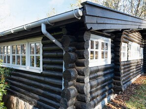 Eine Blockhütte mit Satteldach und zwei Fenstern mit weißen Rahmen.