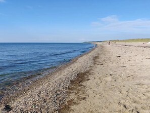 Una playa pedregosa con agua cristalina y una lejana vista de colinas.