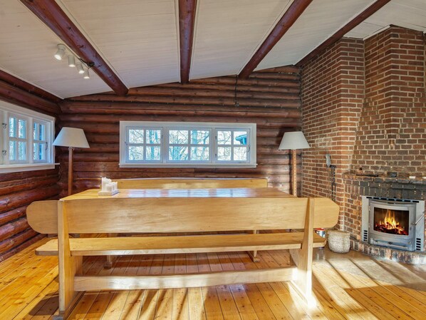 A log cabin interior with a wooden bench, a fireplace, and a window with a view of trees.