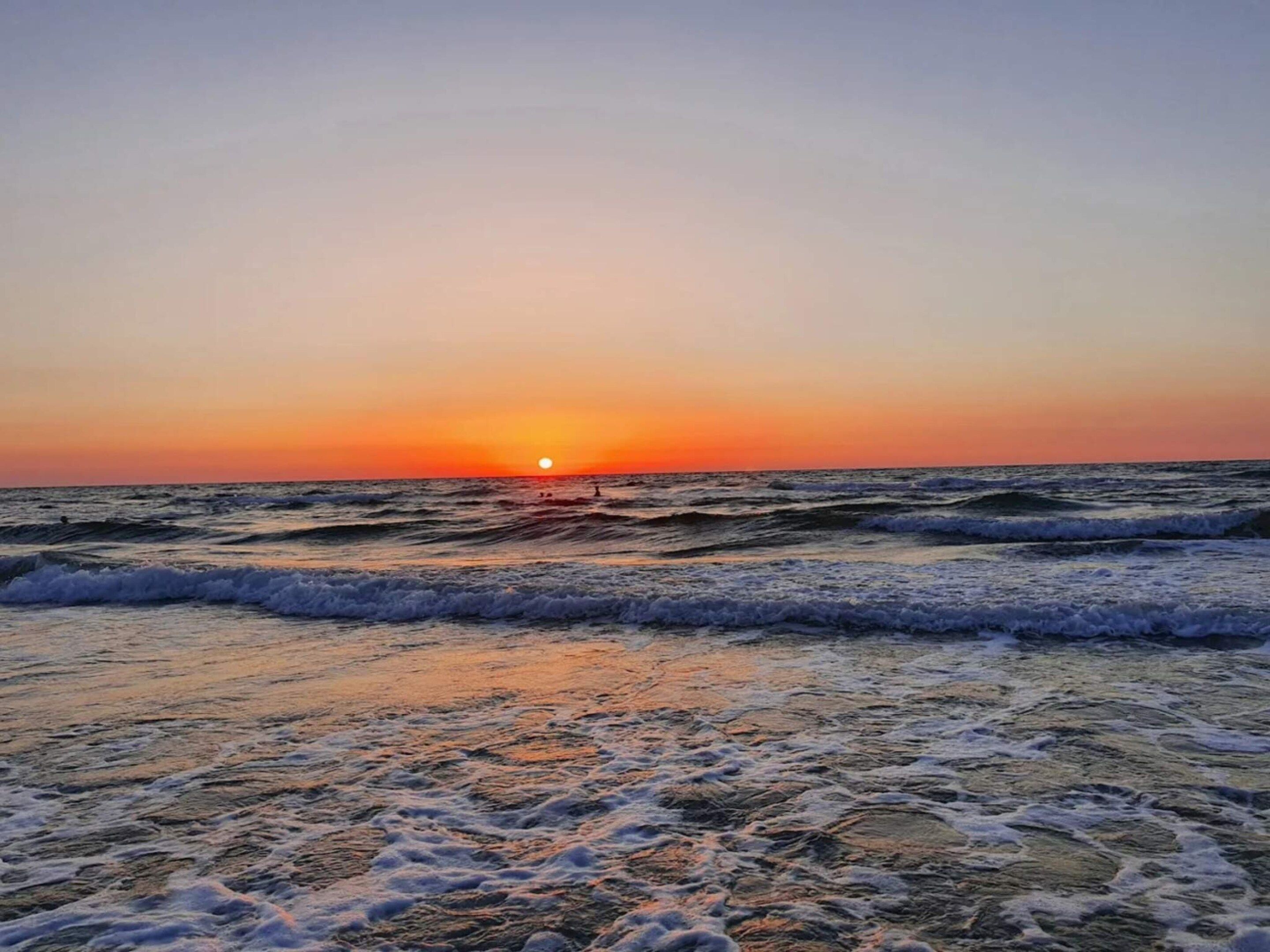 Una playa al atardecer con olas y un cielo despejado.