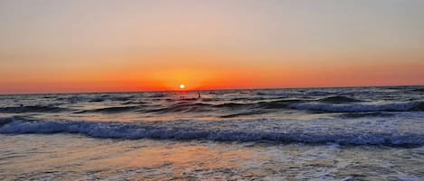 Une plage au coucher du soleil, avec des vagues et un ciel dégagé.