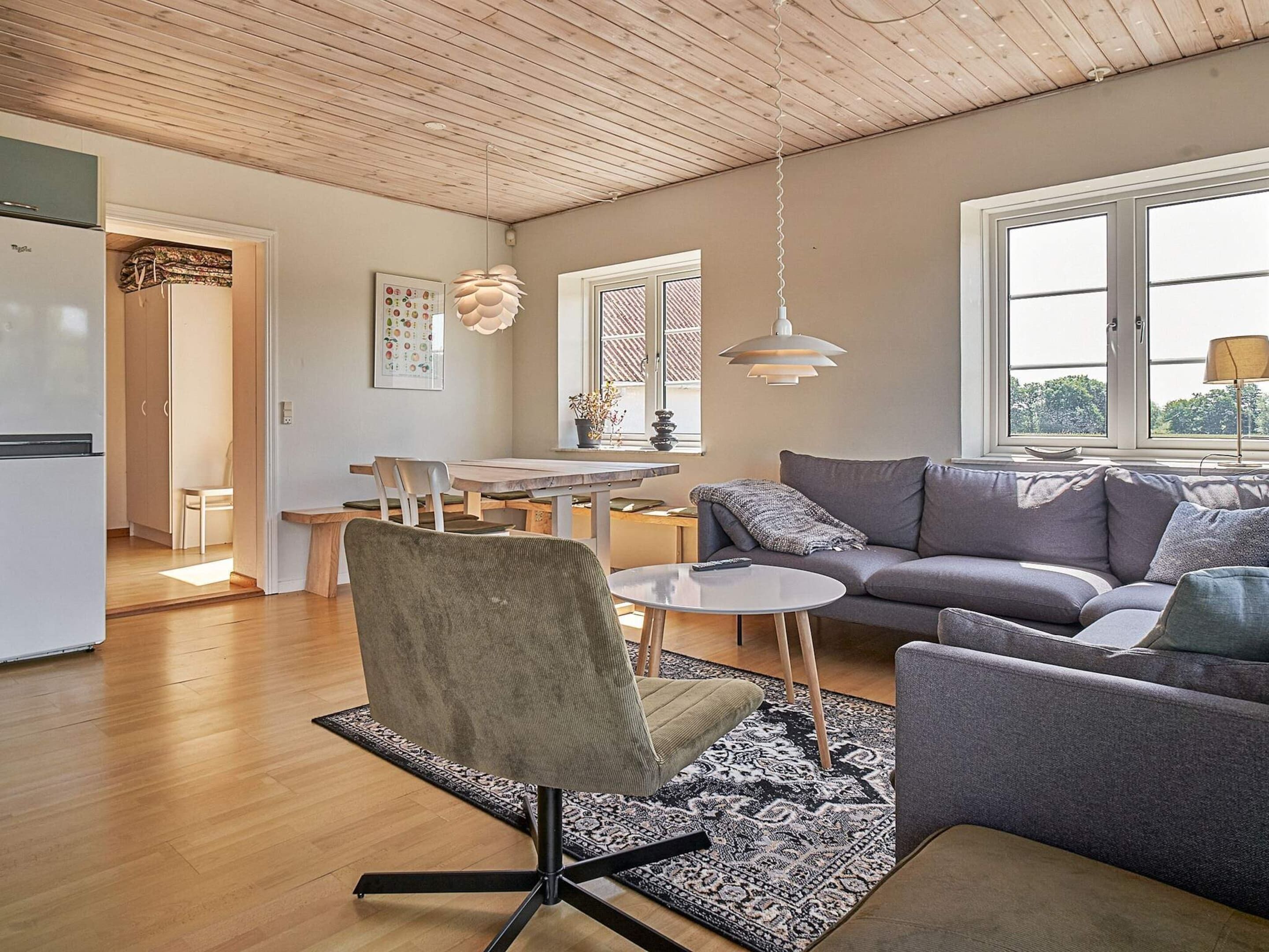 En moderne stue med en grå sofa, et rundt sofabord og et spiseområde med et træbord og stole.