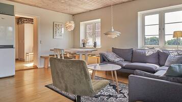 En moderne stue med en grå sofa, et rundt sofabord og et spiseområde med et træbord og stole.