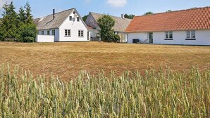 A white building with a red-tiled roof, a grassy field in front, and a wheat field in the foreground. - 12 Person Holiday Home in Aakirkeby (Akirkeby)