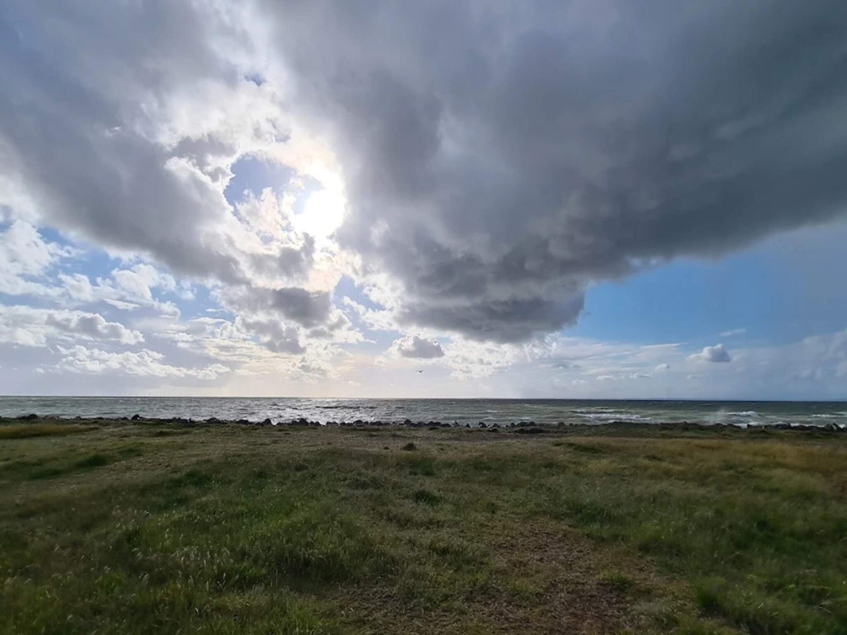 Un campo cubierto de césped con vista al océano y un cielo nublado.