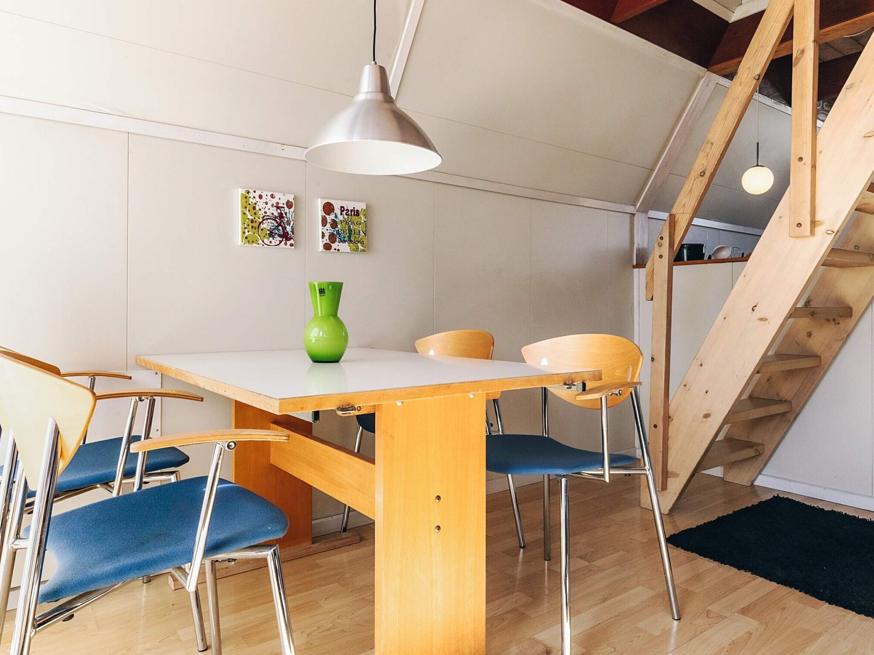 Un comedor con una mesa y sillas de madera, un jarrón verde y dos lámparas colgantes fijadas a la pared.